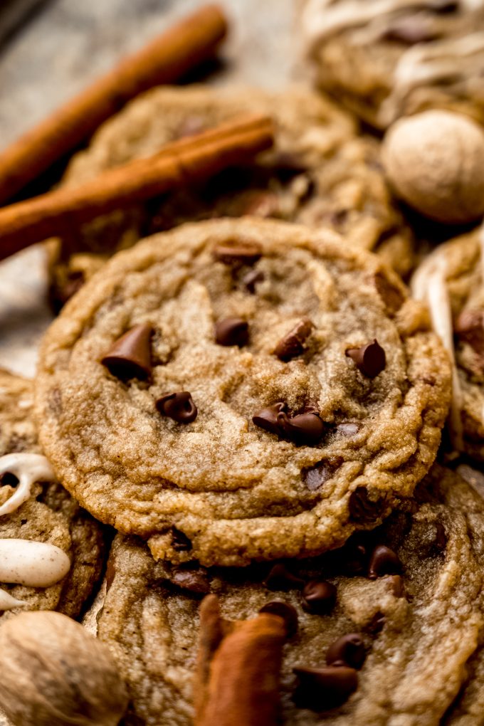 Spiced chocolate chip cookies on a surface with whole nutmeg and cinnamon sticks around it.