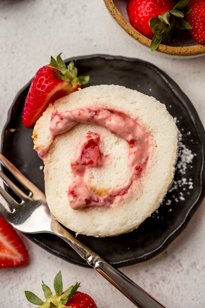 A slice of strawberry Swiss roll cake on a plate with a fork.