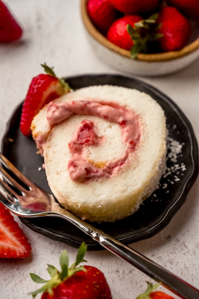 A slice of strawberry Swiss roll cake on a plate with a fork.