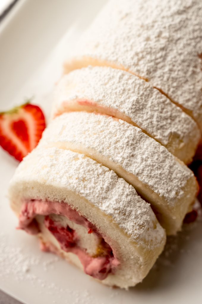 A strawberry Swiss roll cake on a plate with strawberries around it.
