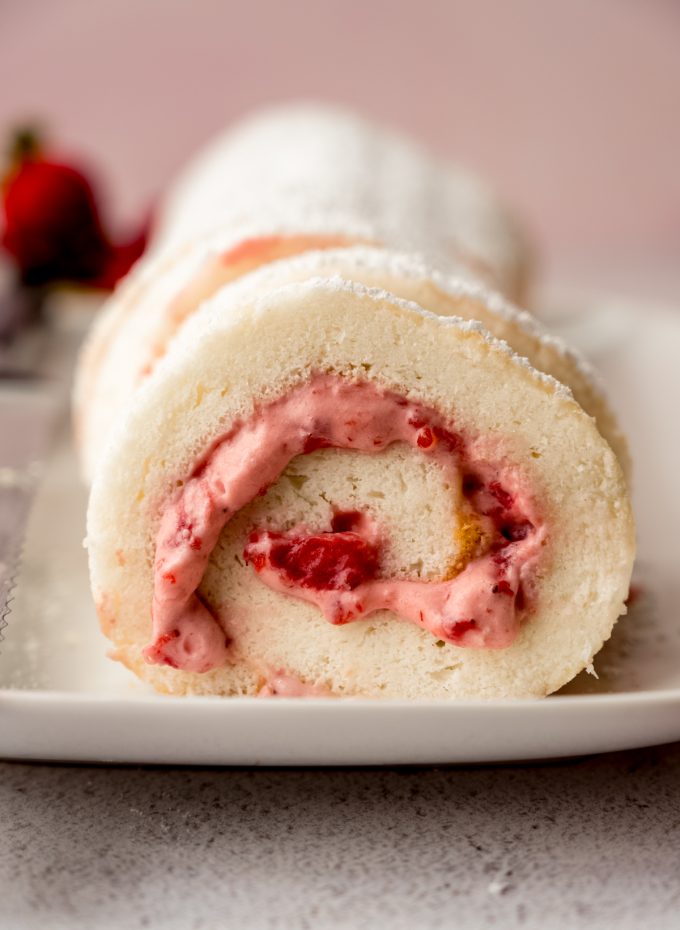 A strawberry Swiss roll cake on a plate with strawberries around it.