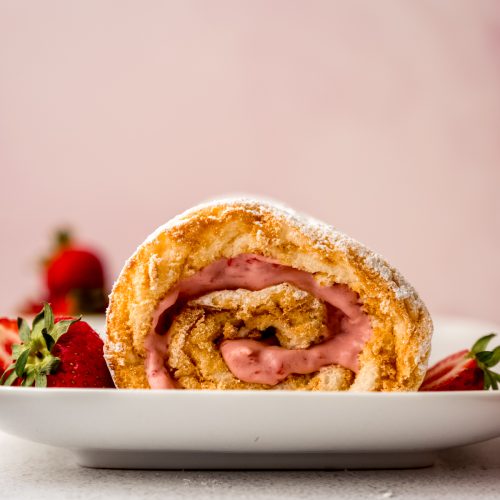 A strawberry Swiss roll cake on a plate with strawberries around it.