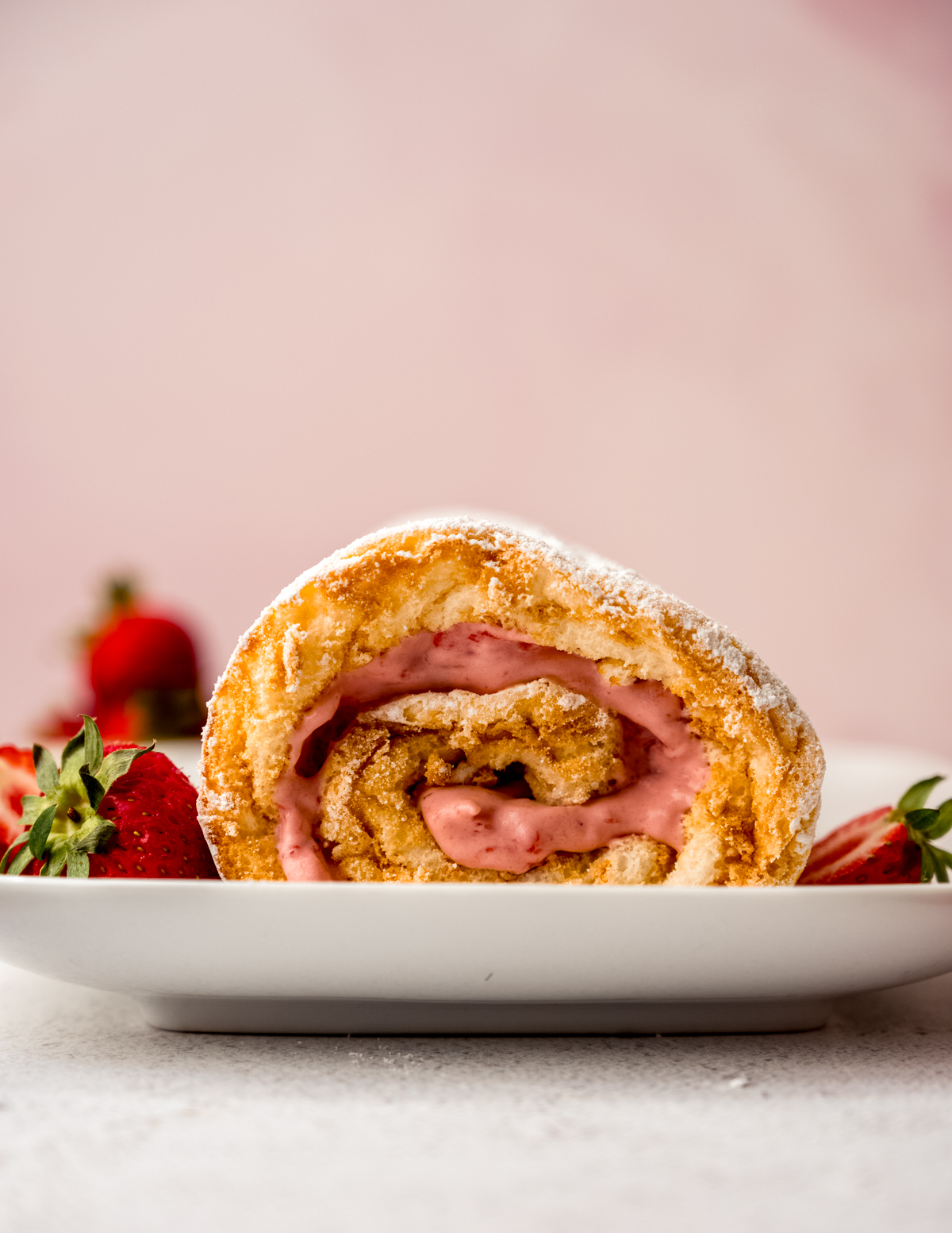 A strawberry Swiss roll cake on a plate with strawberries around it.