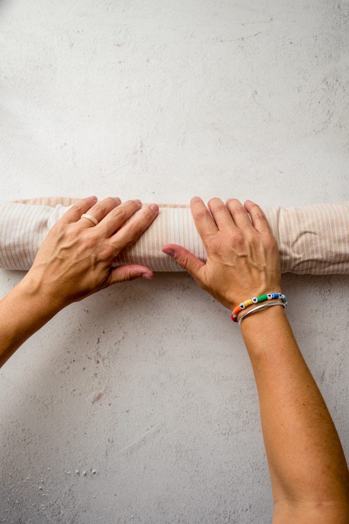 Someone is rolling up a layer of cake into a kitchen towel to make a Swiss roll cake.
