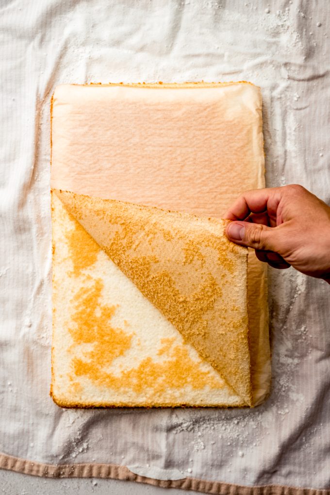 Someone is pulling the parchment off of a layer of cake to make a Swiss cake roll.