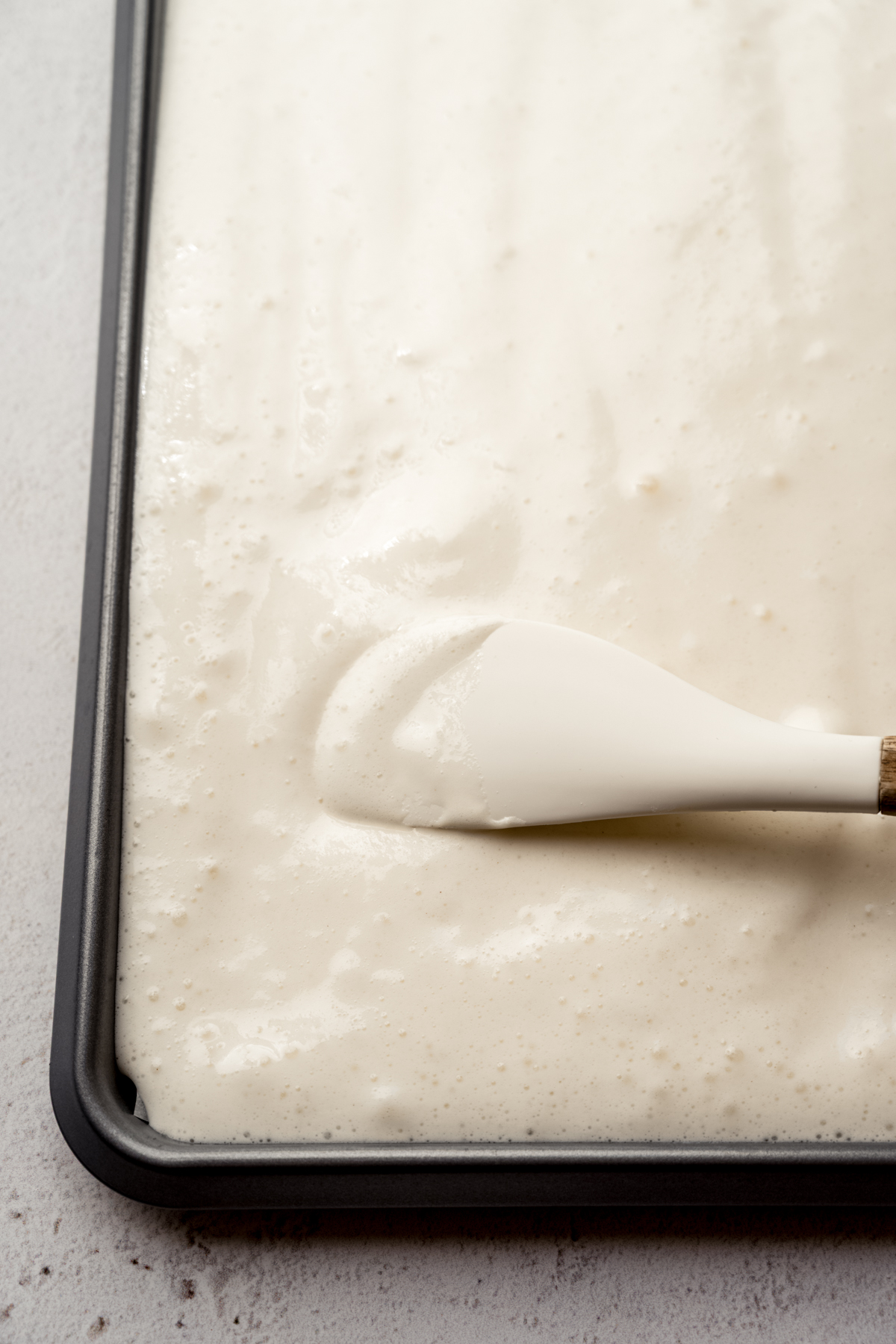 Someone is using a spatula to spread cake batter into a jelly roll pan.