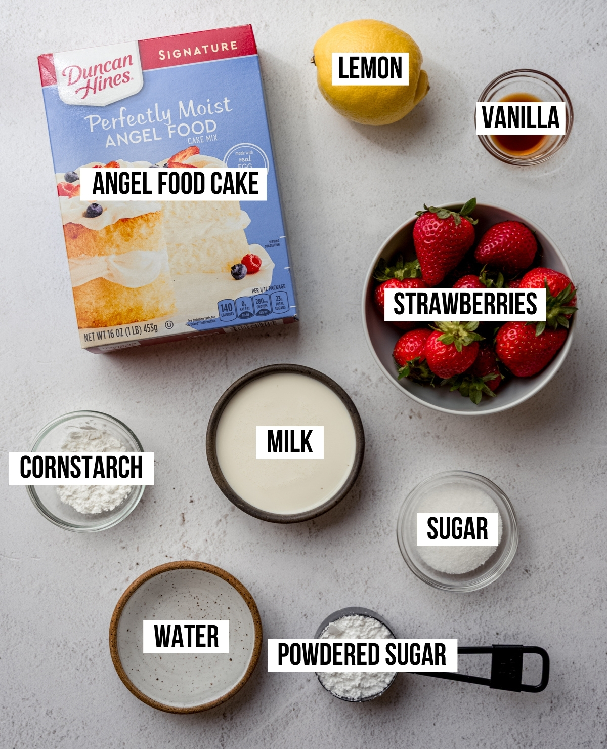 Aerial photo of ingredients to make a strawberry Swiss roll cake with text overlay labeling each ingredient.