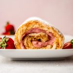 A strawberry Swiss roll cake on a plate with strawberries around it.