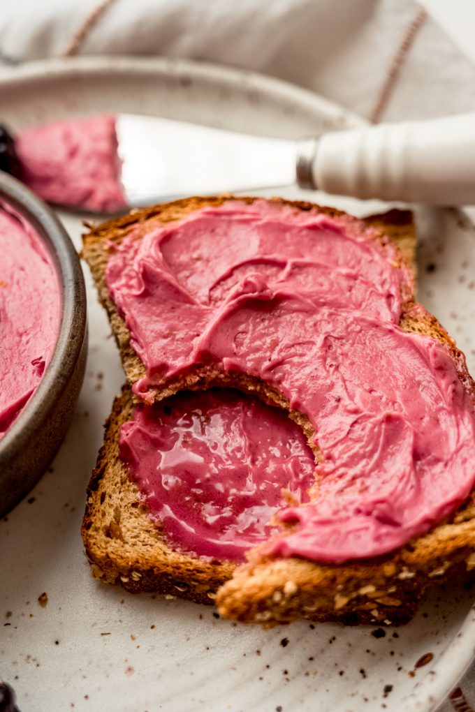 A slice of toast spread with blackberry butter and a bite has been taken out of one of the pieces of the toast.