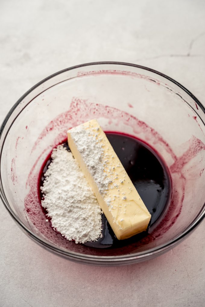 A glass bowl with blackberry juice, powdered sugar, and butter in it.
