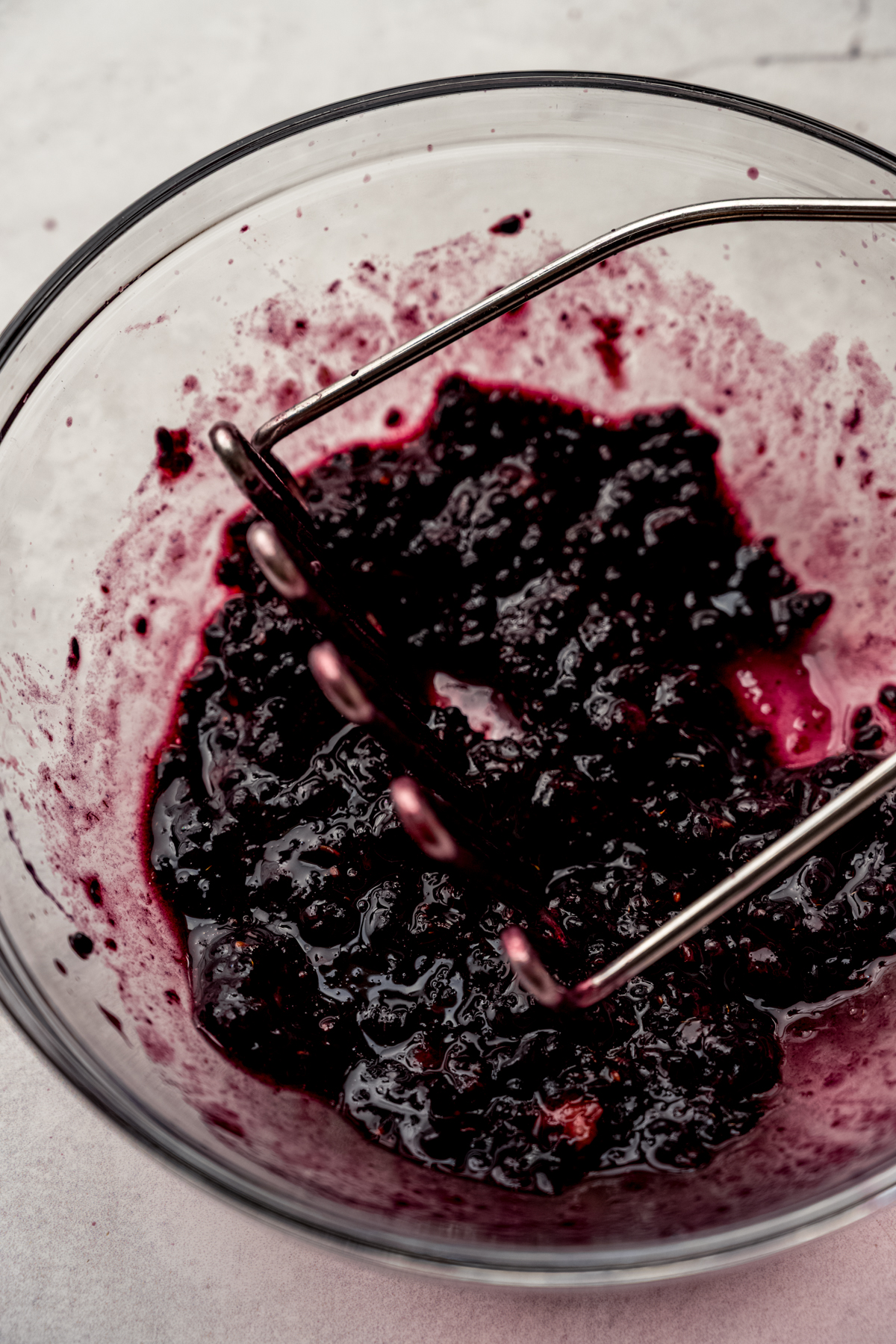 Blackberries in a bowl being macerated with a potato masher.