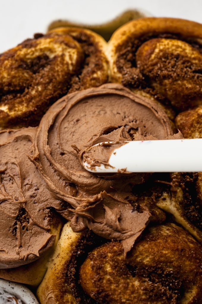 Someone is using a spatula to spread Nutella frosting onto Nutella rolls.