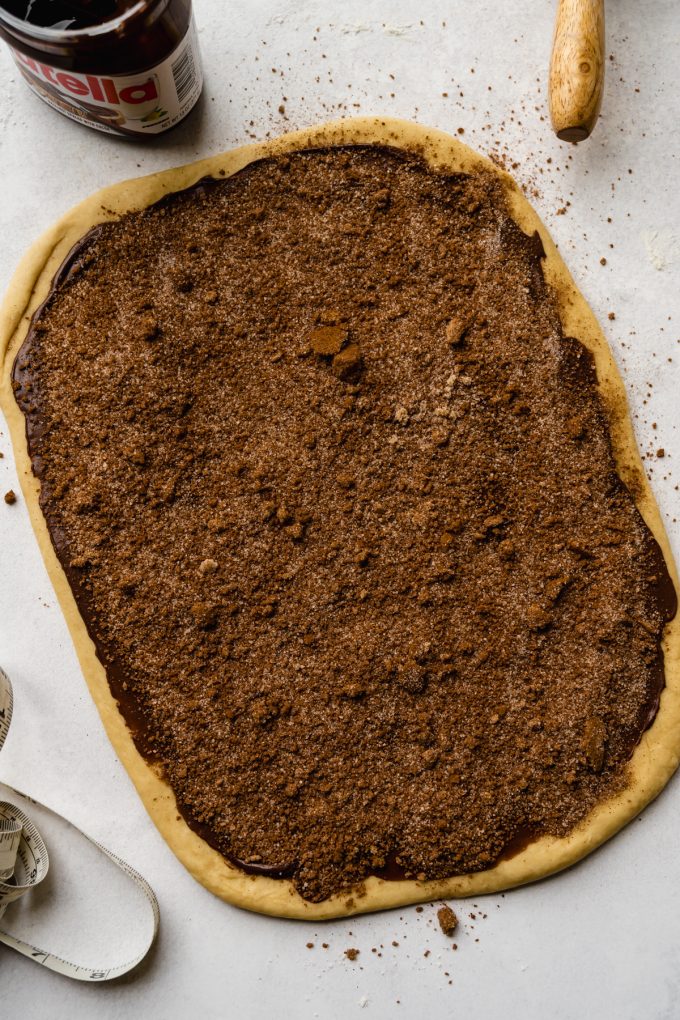 Aerial photo of a rectangle of dough with Nutella and cinnamon roll dough filling on it ready to be rolled up into a log.