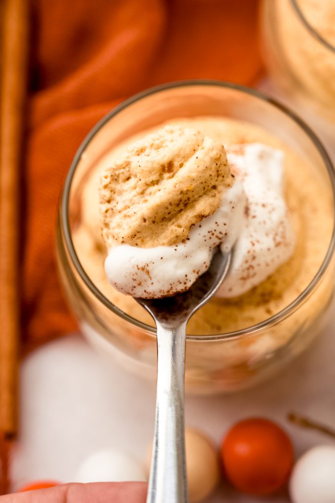 A spoonful of pumpkin mousse being held over a dessert cup.