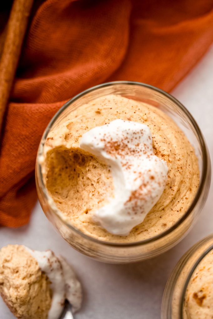 A dessert cup of pumpkin mousse with a spoonful taken out of it.