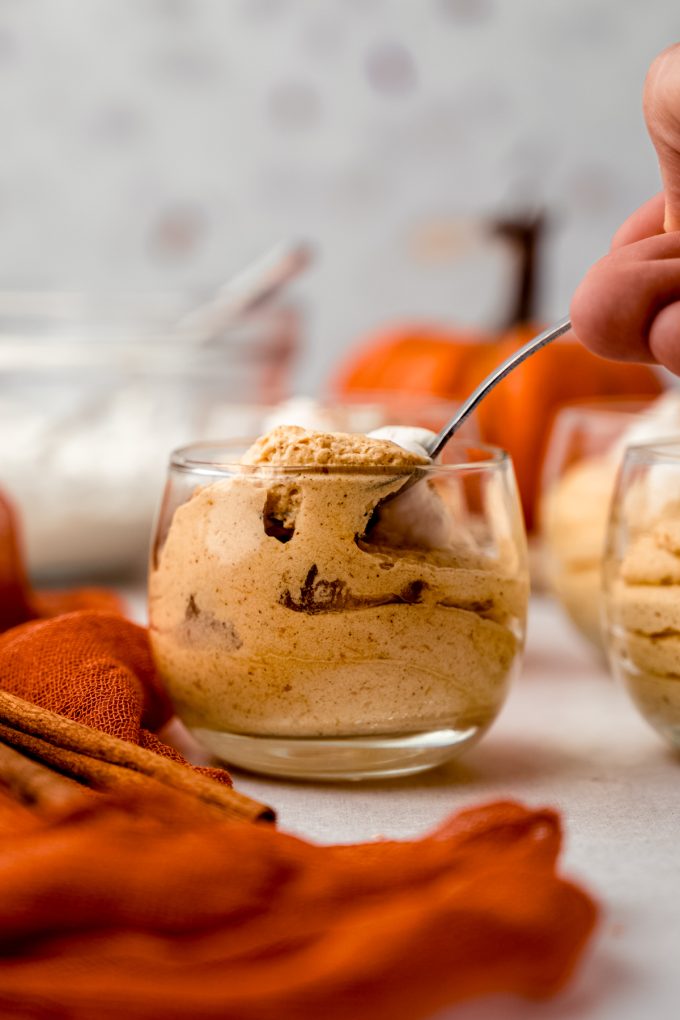 Someone is putting a small spoon into a dessert cup of pumpkin mousse.