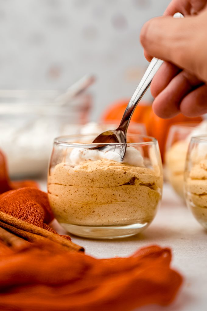 Someone is putting a small spoon into a dessert cup of pumpkin mousse.