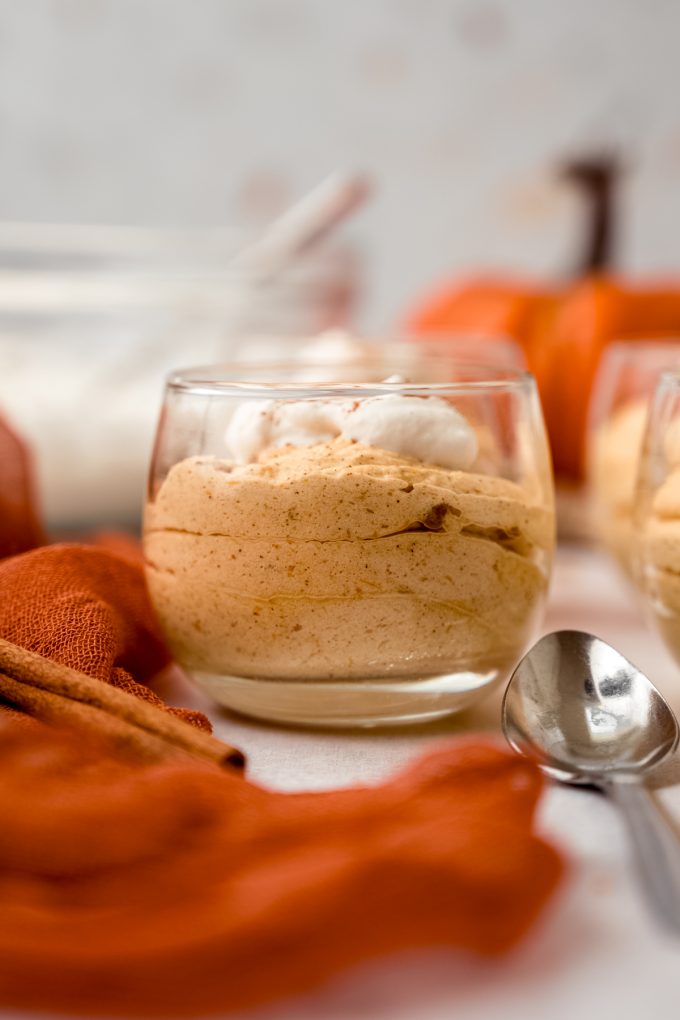 A dessert cup filled with pumpkin mousse and a spoon resting next to it.