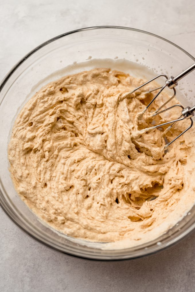 Pumpkin mousse in a large glass bowl with electric beaters.