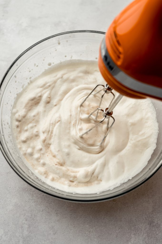 Someone is using an electric mixer to make pumpkin mousse in a large glass bowl.