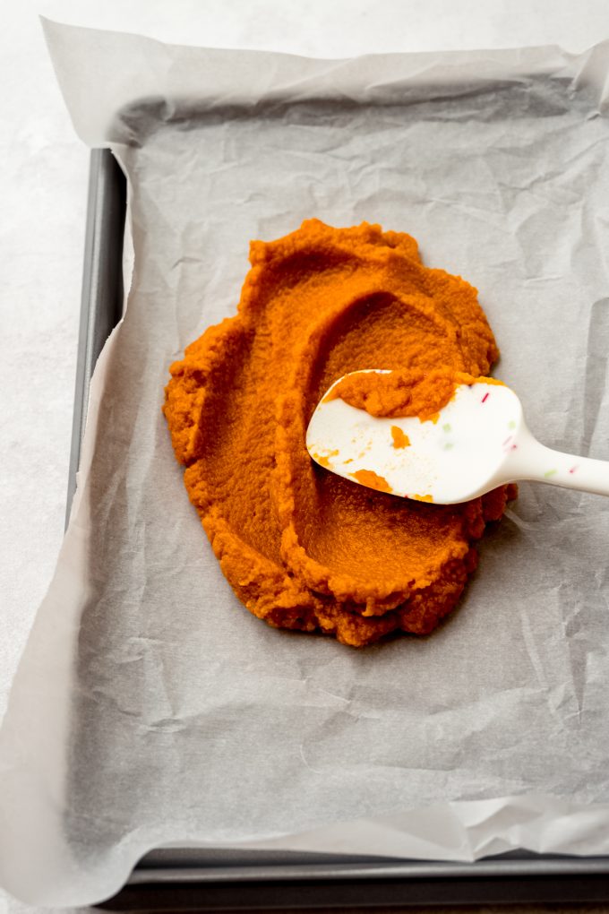 Someone is spreading pumpkin puree onto a baking sheet.