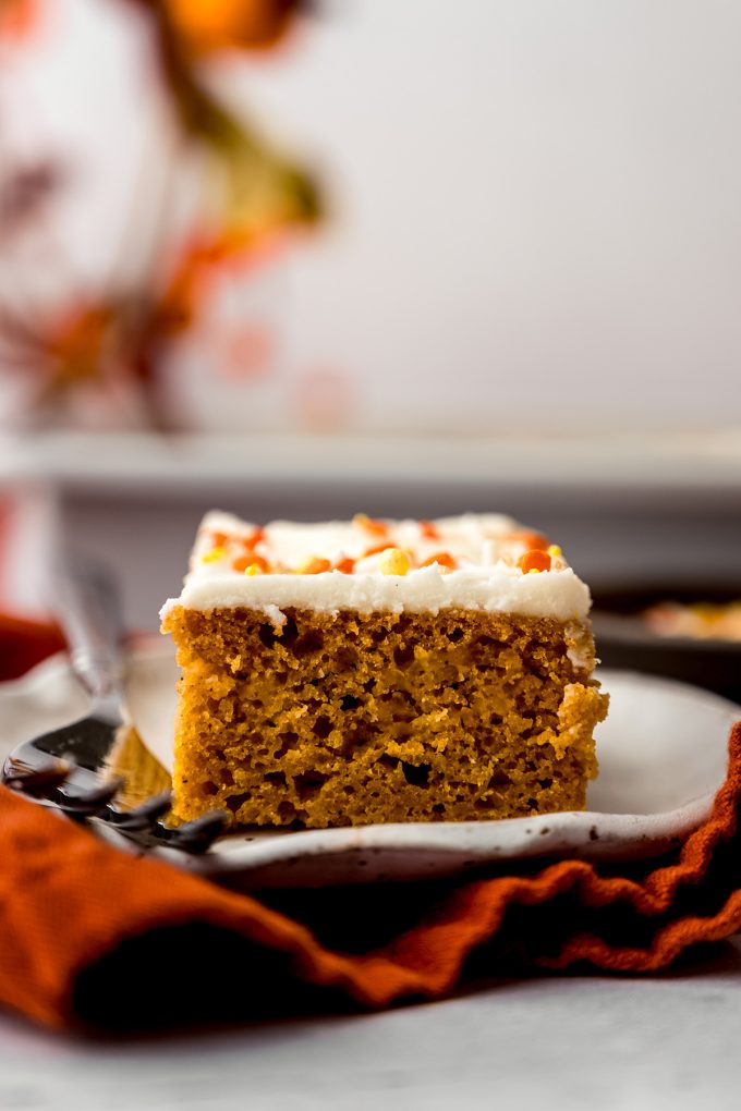 A slice of pumpkin sheet cake sitting on a plate with a fork.