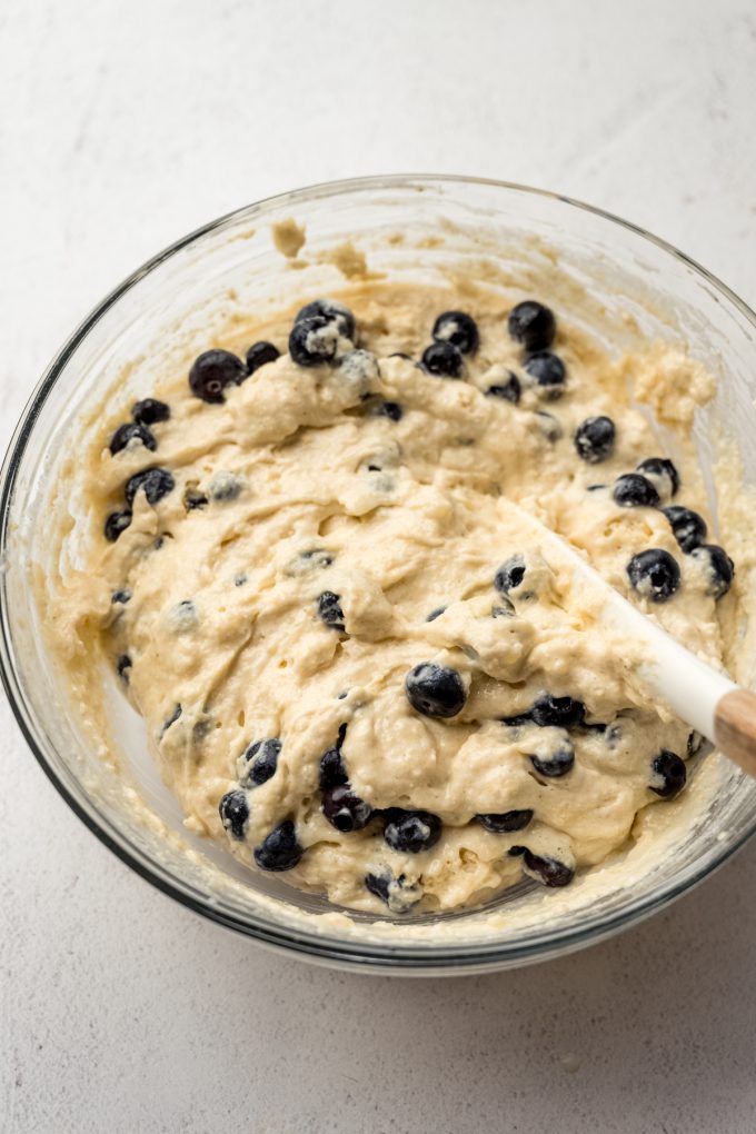 Someone is stirring a bowl of blueberry cornbread batter with a spatula.