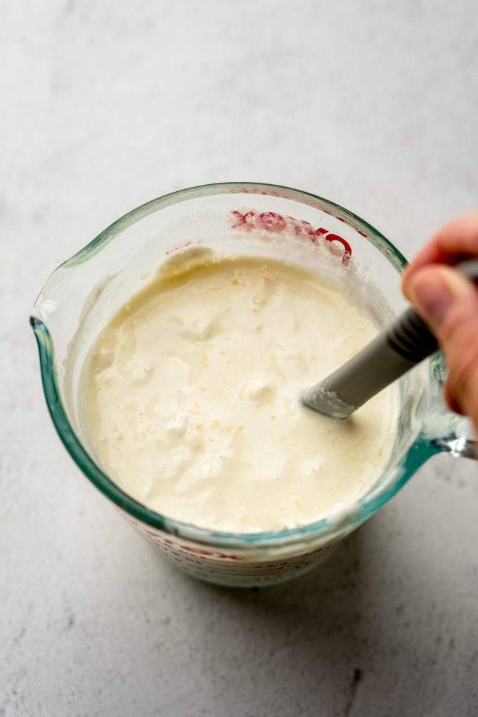 Someone is stirring the wet ingredients for cornbread in a large measuring cup.
