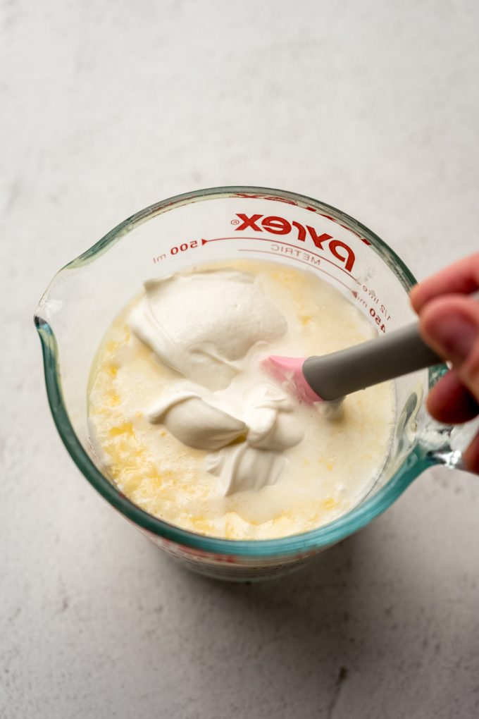 Someone is stirring the wet ingredients for cornbread in a large measuring cup.
