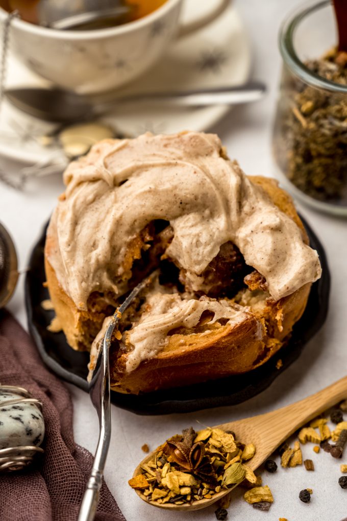 Someone is cutting into a chai cinnamon roll with a fork on a plate.