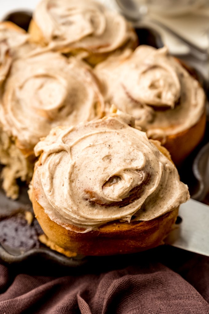 Someone is lifting a chai cinnamon roll out of a baking dish with a spatula.