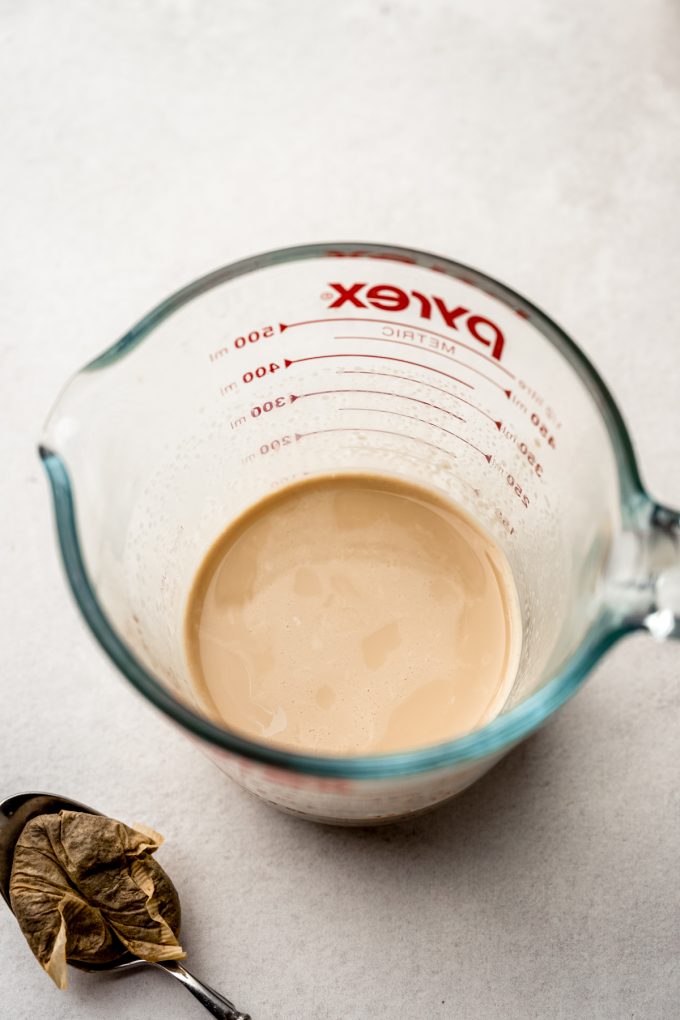 A measuring cup with chai-infused milk in it and a spoon and used tea bag off to the side.