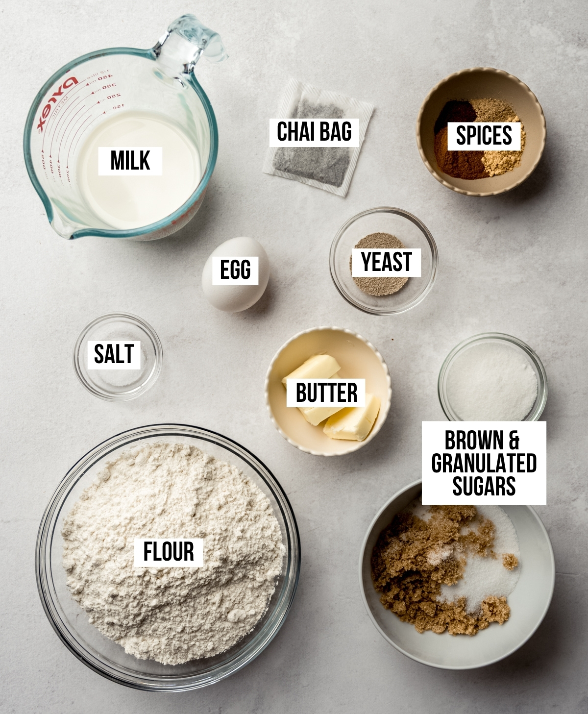 Aerial photo of ingredients to make chai cinnamon rolls with text overlay labeling each ingredient.