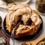 Someone is cutting into a chai cinnamon roll with a fork on a plate.