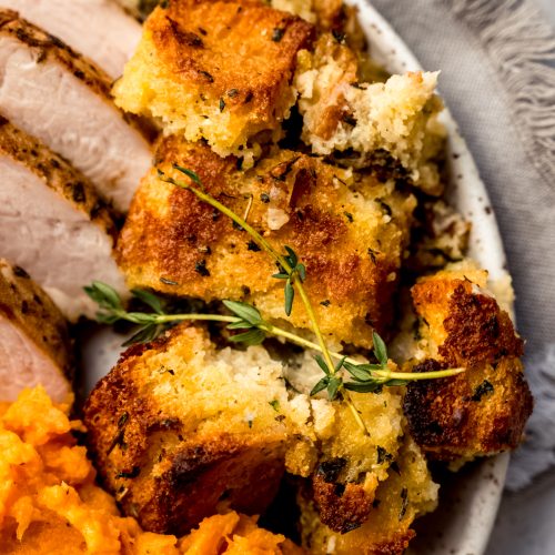 Cornbread stuffing on a plate with a fresh thyme sprig.