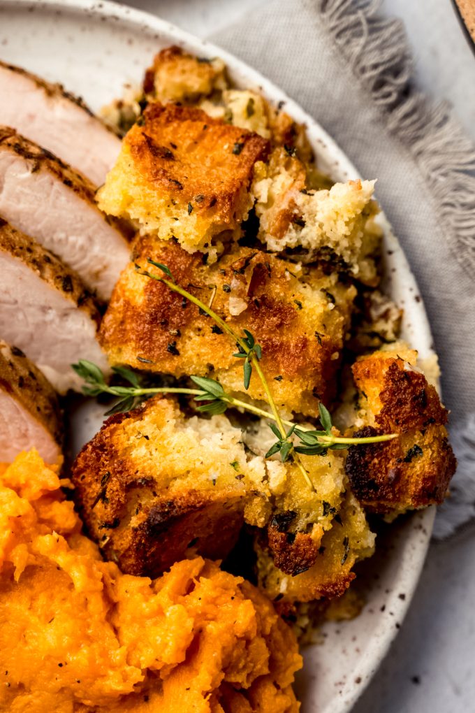 Cornbread stuffing on a plate with turkey and mashed sweet potatoes and a sprig of fresh thyme.