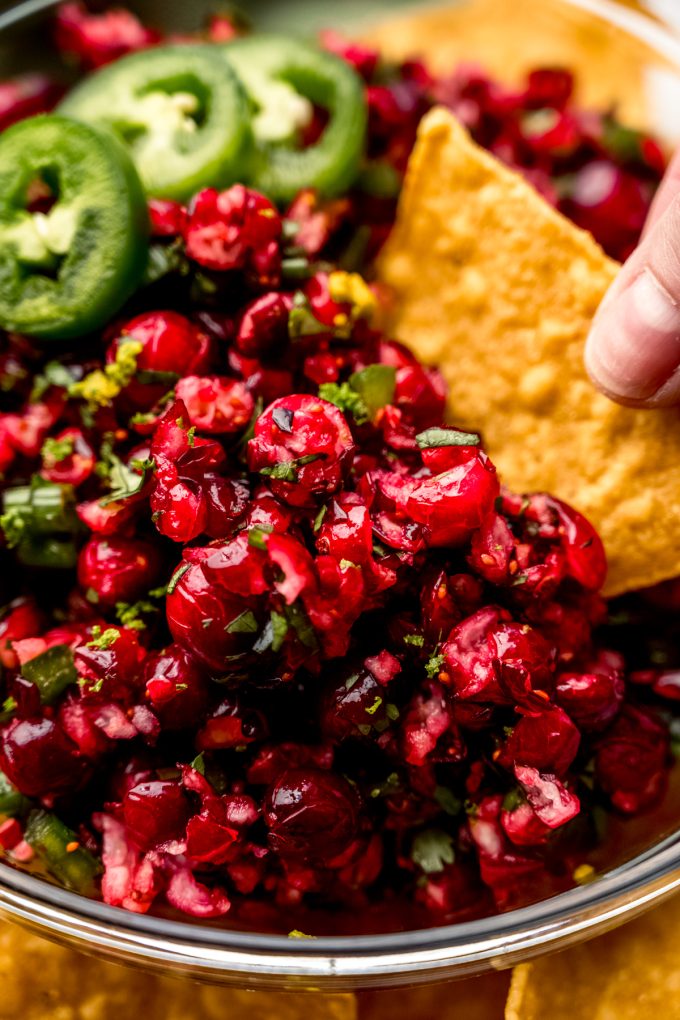 Someone is using a chip to dip into cranberry salsa.