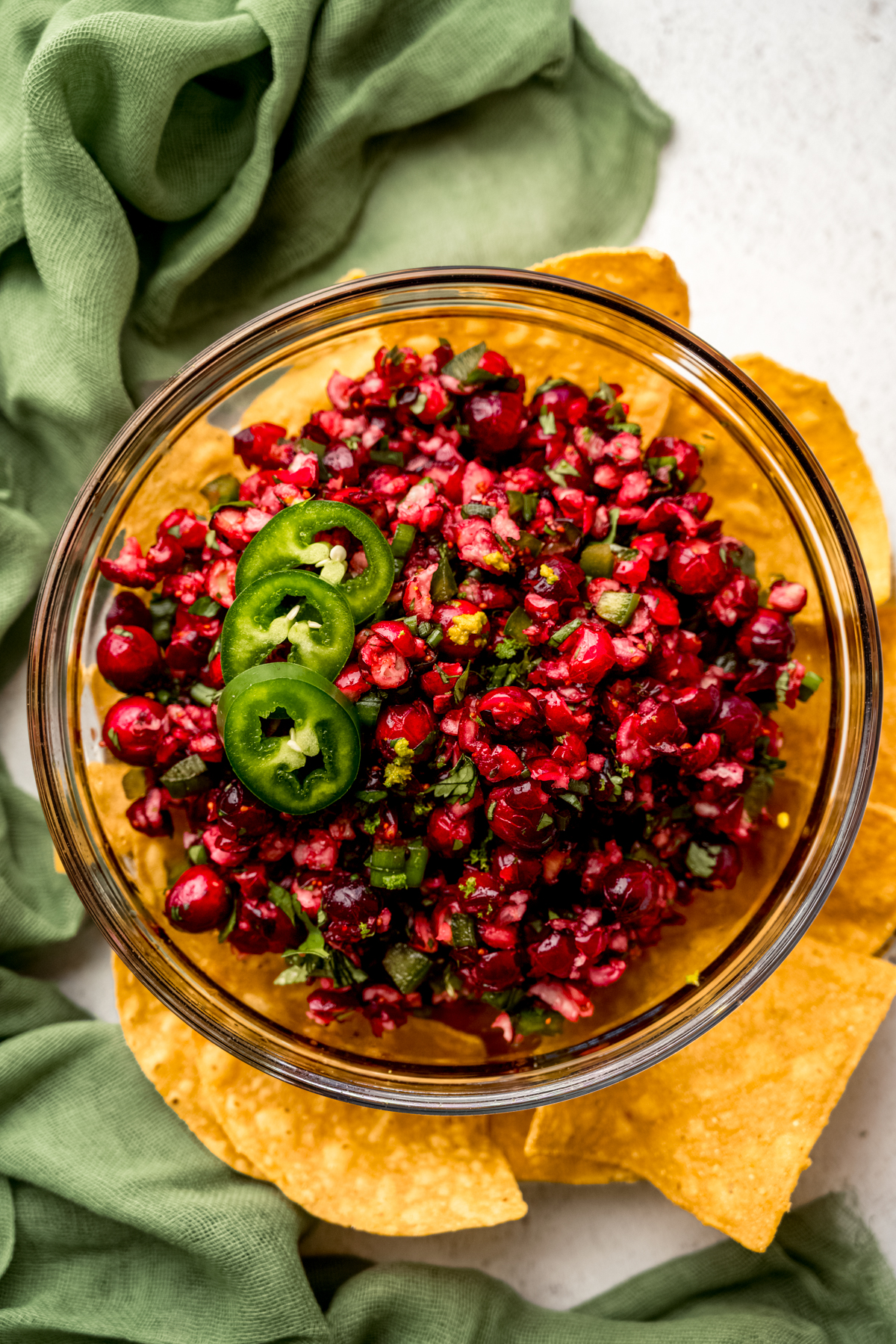 Aerial photo of a bowl of cranberry salsa in the middle of a plate of chips.