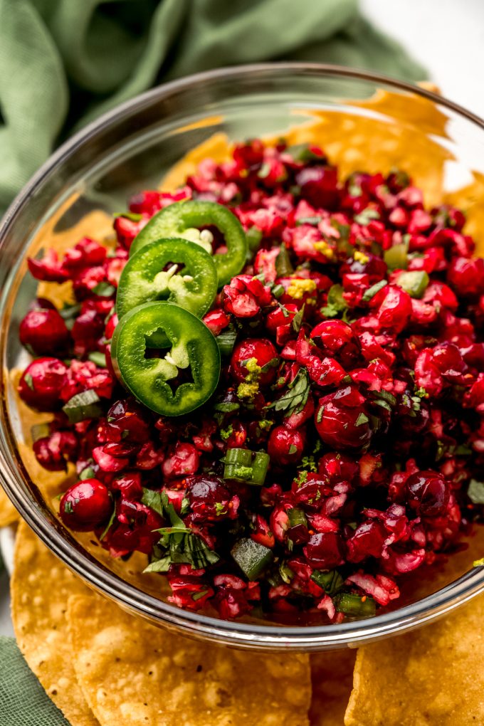 A bowl of cranberry salsa in the middle of a plate of chips.