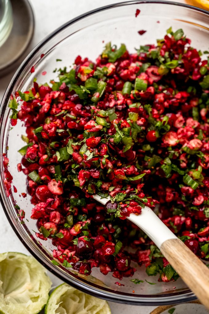 Someone is stirring a bowl of chopped cranberries and other ingredients to make cranberry salsa.