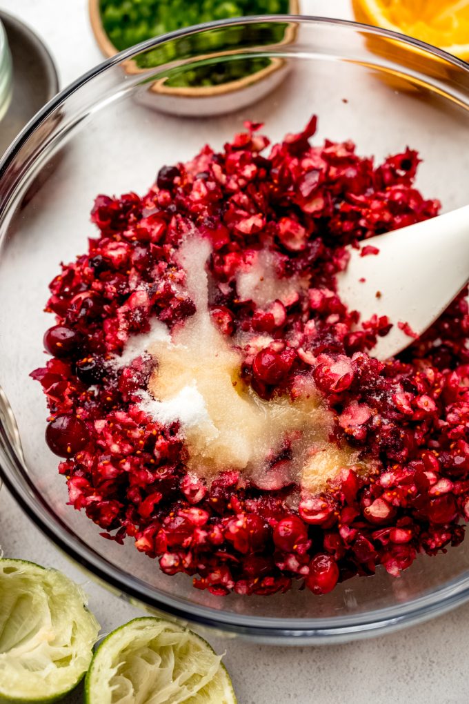 A bowl of chopped fresh cranberries, sugar, and some citrus juices and a spatula in it.