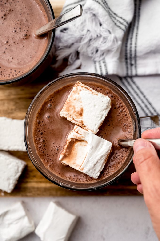 Aerial photo of someone stirring a mug of hot chocolate and marshmallows with a spoon.