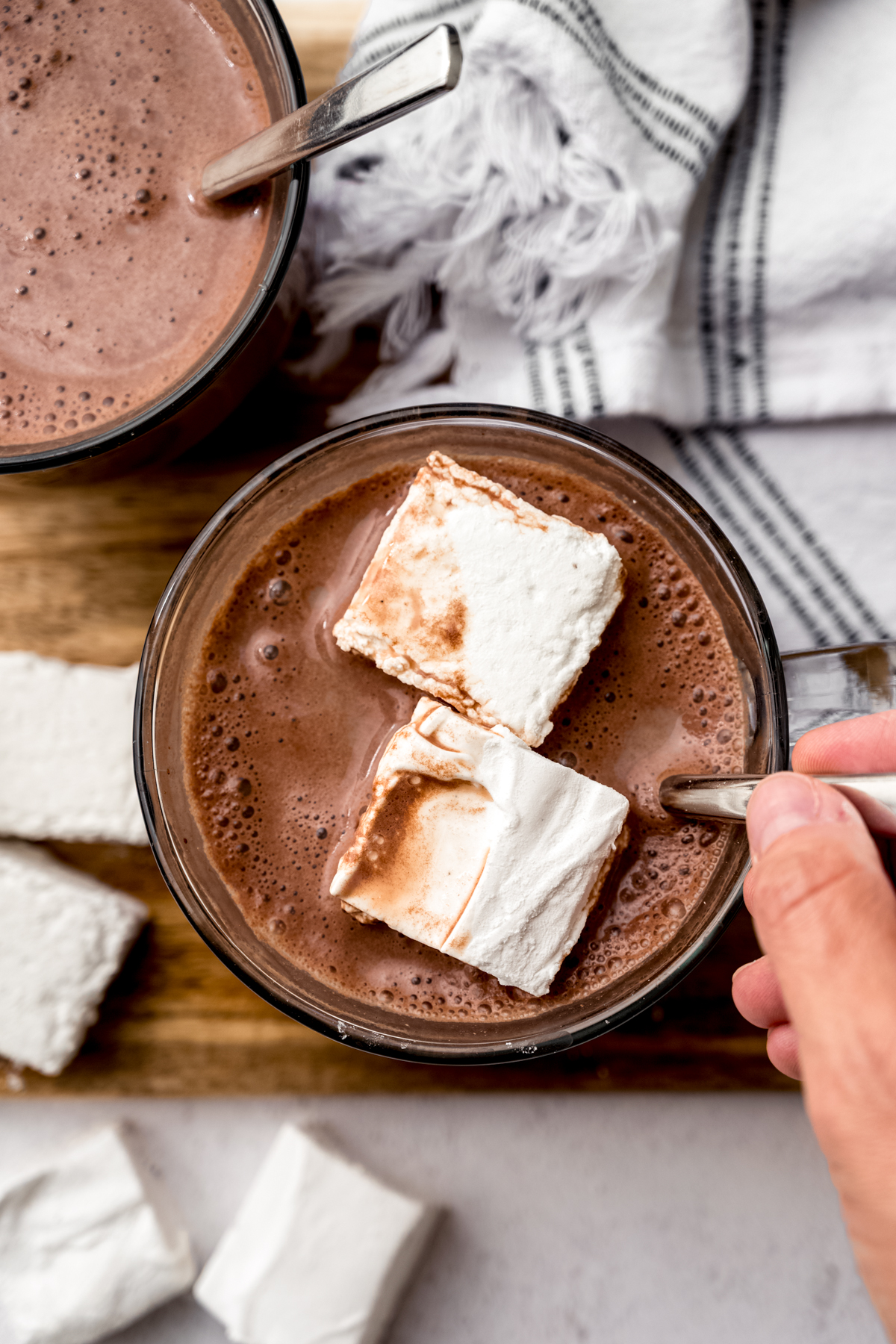 Aerial photo of someone stirring a mug of hot chocolate and marshmallows with a spoon.
