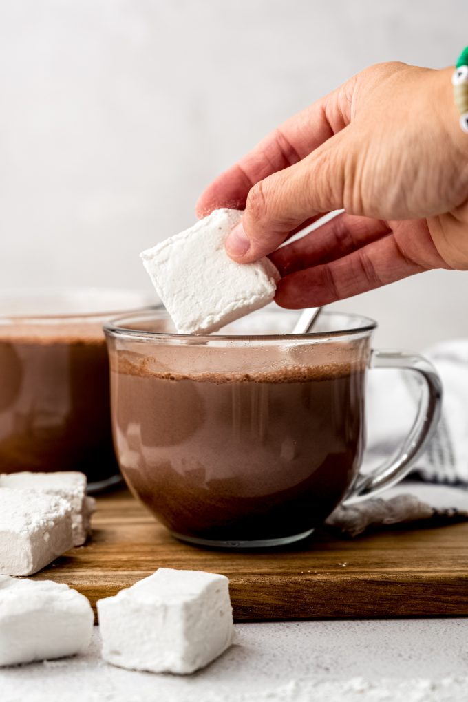 Someone is dropping a homemade marshmallow into a mug of hot chocolate.