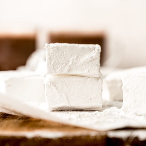 Two homemade marshmallows in a stack on a surface.