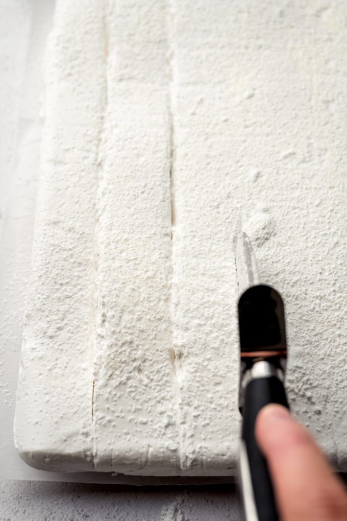 Someone is using a pizza cutter to cut a block of homemade marshmallows.