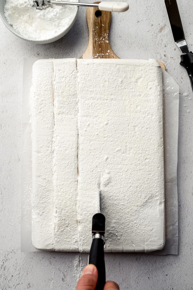 Aerial photo of someone using a pizza cutter to cut a block of homemade marshmallows.