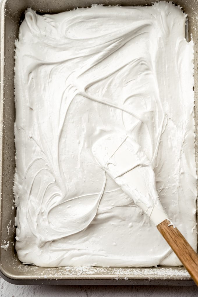 Someone is spreading homemade marshmallow mixture into a baking pan.