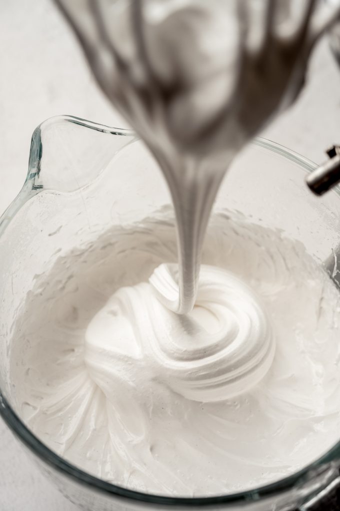 Someone is pulling the whisk attachment out of a bowl of homemade marshmallow mix.