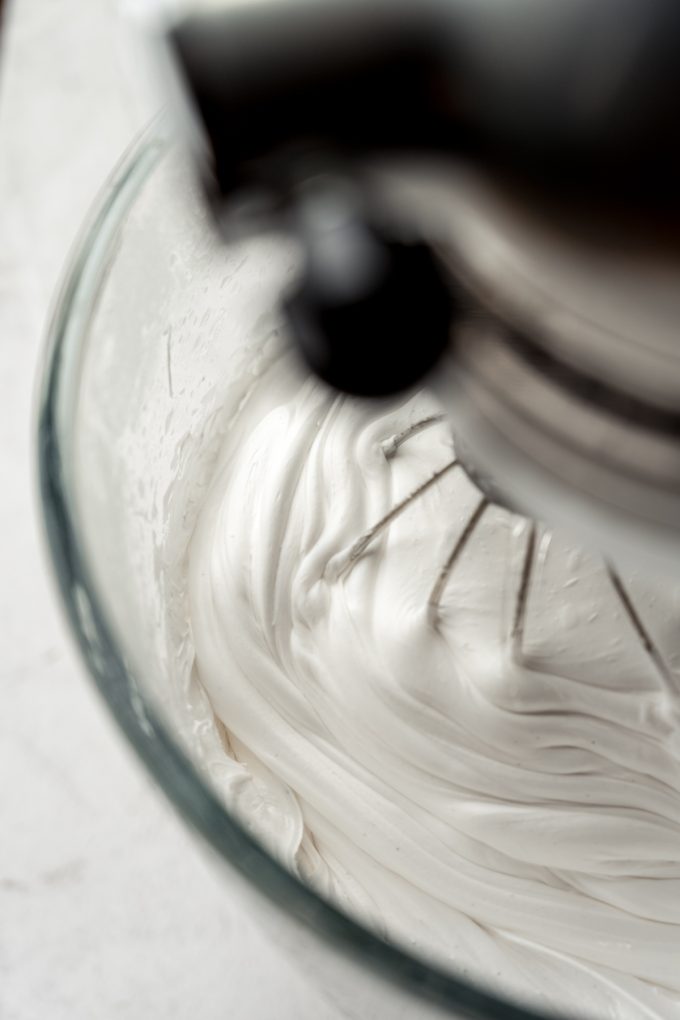 A mixer with homemade marshmallow mixture in the bowl with the whisk attachment.
